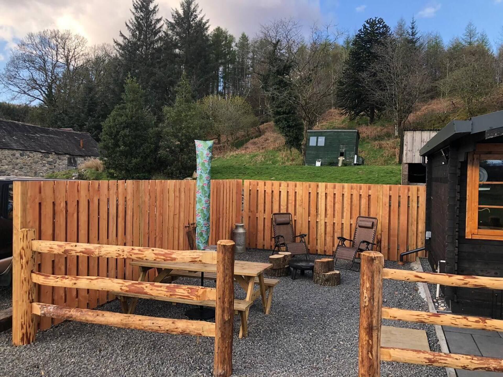 A rustic outdoor seating area with wooden benches and tables, surrounded by a wooden fence.