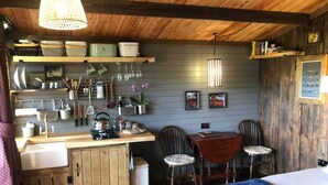 A compact kitchen with wooden cabinets, a dining table with chairs, and a bed with a blue blanket. - 1 Bed Cabin in the Magical Galloway Forest Park (Newton Stewart)