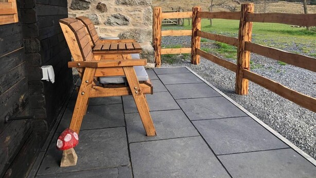 A wooden bench with cushions outside a stone building, a wooden fence, and a mountain in the background. - 1 Bed Cabin in the Magical Galloway Forest Park (Newton Stewart)