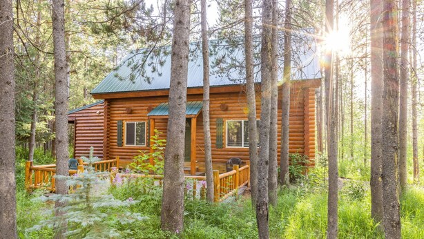 Eine Blockhütte, umgeben von hohen Bäumen, mit Veranda und Gartenmöbeln.