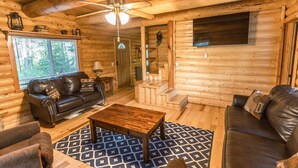 Ein Holzblockhaus-Interieur mit einem Ledersofa, einem Holztisch und einem gemusterten Teppich.
