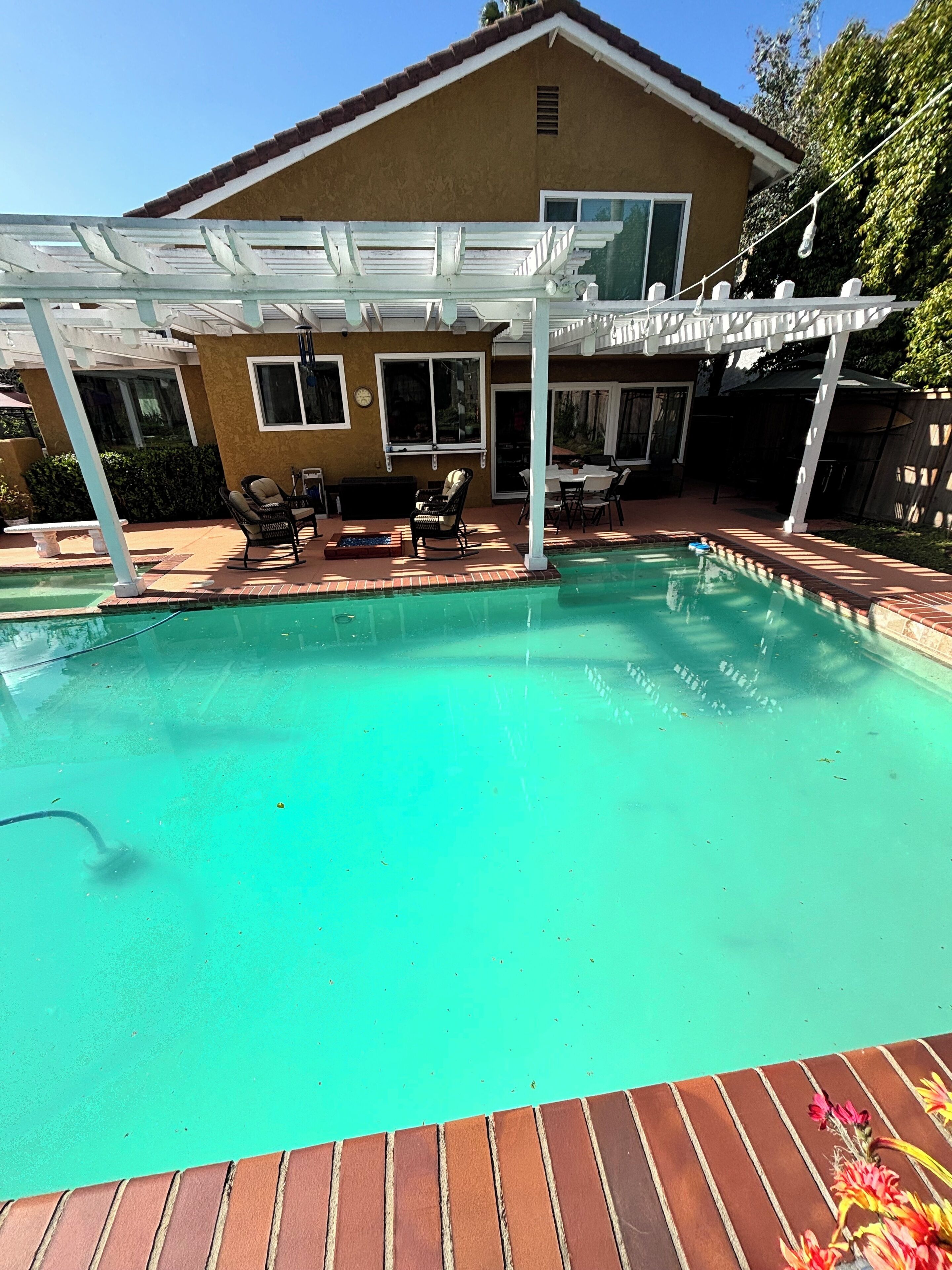 A backyard with a swimming pool, a covered patio area, and a house with a brown exterior.