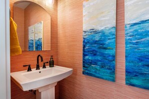 Un baño con un lavabo blanco, grifos negros y una toalla amarilla colgada en la pared.