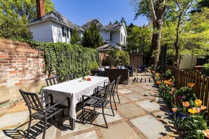 Un patio con una mesa lista para comer, rodeado de sillas y un muro de ladrillo.
