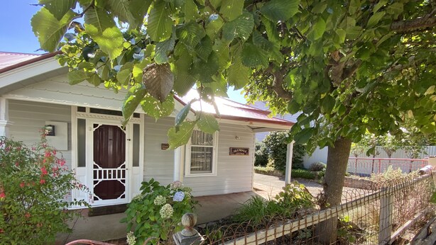 Una cabaña blanca con un porche, un letrero que dice "Glendale Cottage" y un jardín cercado.