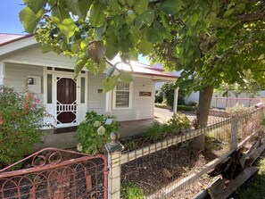 Guesthouse with a classic design, featuring a front porch and garden area, surrounded by a fence.