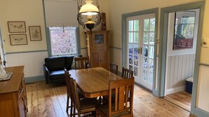 Un comedor con una mesa y sillas de madera, una araña y vistas al exterior por un ventanal.