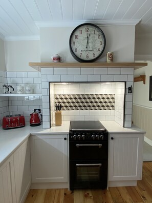 Kitchen features a central island with a stove and oven, white cabinetry, and a geometric-patterned backsplash.