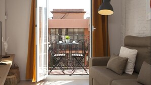 Ein modernes Wohnzimmer mit einer Couch, einem Tisch mit Stühlen, einem Balkon mit Geländer und einer Pendelleuchte.