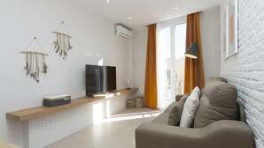 Ein modernes Wohnzimmer mit einer Couch, einem Flachbildfernseher, einem Holzregal und einer Wand-Klimaanlage.
