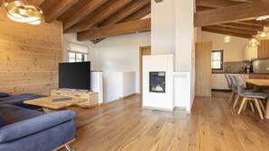 A modern living room with a wooden ceiling, a fireplace, a dining area, and a kitchen.
