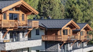 A multi-story wooden chalet with balconies, stone foundations, and a car parked in front.