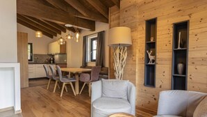 A cozy cabin interior with a wooden dining area, two grey sofas, a lamp, and a decorative shelf.