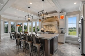 Une cuisine spacieuse dotée d’un grand îlot central, d’appareils électroménagers modernes et de grandes fenêtres offrant une vue sur l’extérieur.