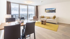 Una sala de estar moderna con comedor, ventanas amplias, un sofá y un cuadro en la pared.