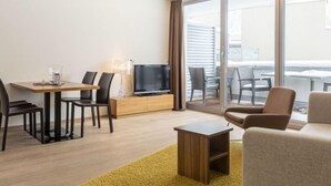 Una habitación de hotel moderna con comedor, televisión de pantalla plana y balcón con mobiliario exterior.