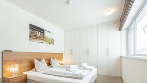 Un dormitorio moderno con cabecera de madera, cama bien tendida, mesita de noche con lámpara y un armario grande.