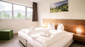 A double bed with white linens and pillows, a wooden headboard, a bedside table with a lamp, a green ottoman, and a window with a view of trees and mountains. - Superior mit 2 Schlafzimmer & Pool by Interhome (Radstadt)
