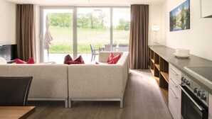 A modern hotel room with a sofa, a dining table, a TV, and a kitchen area. - Superior mit 2 Schlafzimmer & Pool by Interhome (Radstadt)