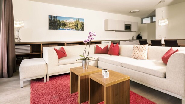 Ein modernes Wohnzimmer mit einem weißen Sofa, roten Kissen, einem Holztisch und einem roten Teppich.