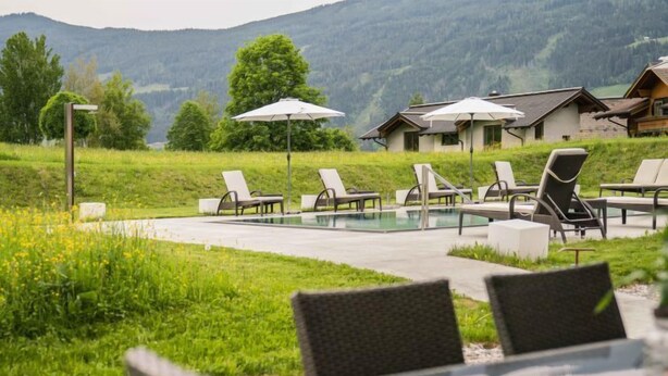 A poolside area with lounge chairs and umbrellas, surrounded by lush greenery and a mountainous backdrop. - Superior mit 2 Schlafzimmer & Pool by Interhome (Radstadt)