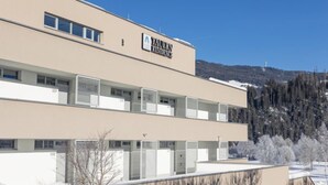 A modern building with a sign reading "YAUER RESIDENCE". It has multiple windows and balconies, with a snowy landscape in the background.