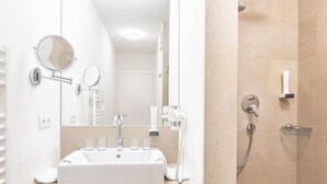 A modern bathroom with a white sink, a mirror, a handheld showerhead, and a towel rack.