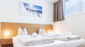 A hotel room with two beds, a wooden headboard, a nightstand with a lamp, and a window with curtains.