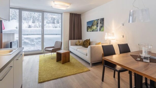 A modern living room with a sofa, a dining table, and a chair. There is a window with a view of a snowy landscape. - 1 Schlafzimmer & Pool by Interhome (Radstadt)