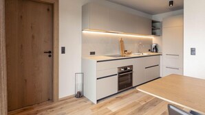 Una cucina moderna con una porta in legno, mobili bianchi, un forno integrato e un tavolo da pranzo in legno.