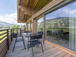 A wooden deck with a table and chairs, large glass windows, and a view of a mountainous landscape.