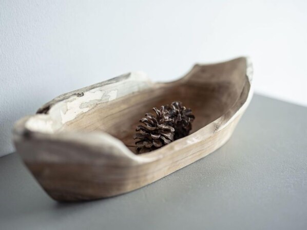 A wooden bowl with a pine cone inside, placed on a grey surface.