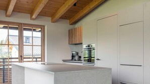 Een moderne keuken met een groot eiland, houten balken in het plafond en uitzicht door een schuifdeur.