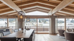 Un'ampia sala da pranzo con un lungo tavolo e sedie, ampie finestre che offrono vista su un paesaggio innevato e un alto soffitto in legno.