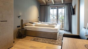 Una camera da letto moderna con soffitto in legno, un letto con lenzuola bianche, un comodino e vista attraverso un'ampia finestra.