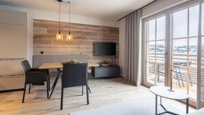 A modern living room with a dining area, large windows, and a flat-screen TV mounted on the wall. - mit 2 Schlafzimmern by Interhome (Westendorf)