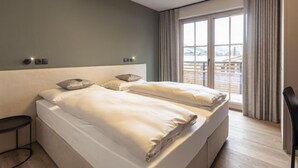 A modern hotel room with a large bed, a bedside table, a chair, and a view of a snowy landscape through the window. - mit 2 Schlafzimmern by Interhome (Westendorf)