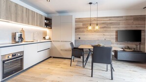A modern kitchen with built-in appliances, a dining area with a table and chairs, and a flat-screen TV mounted on the wall. - mit 2 Schlafzimmern & IR-Sauna by Interhome (Westendorf)