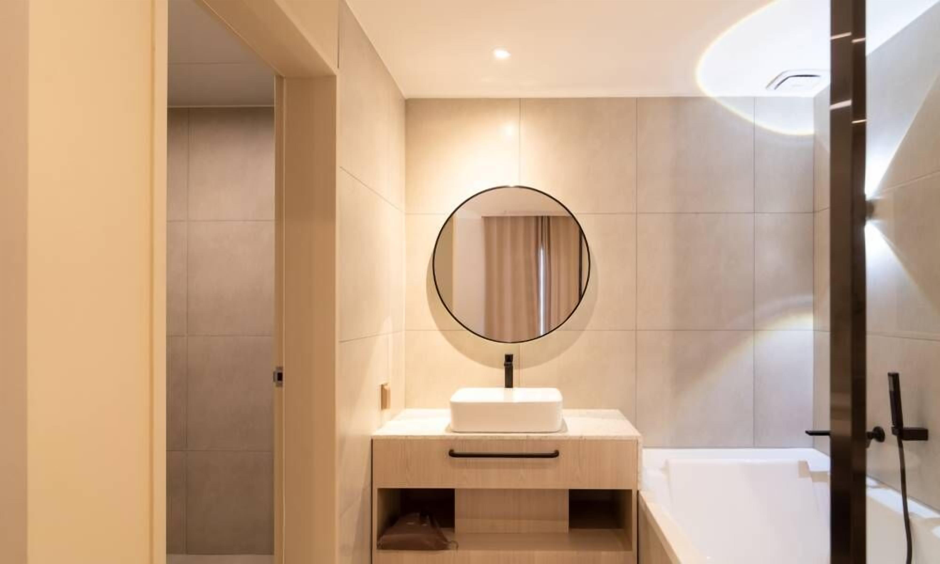 A modern bathroom with a round mirror, a white sink, and a bathtub.