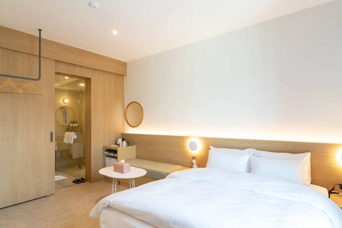 A hotel room with a bed, bedside table, and a mirror.