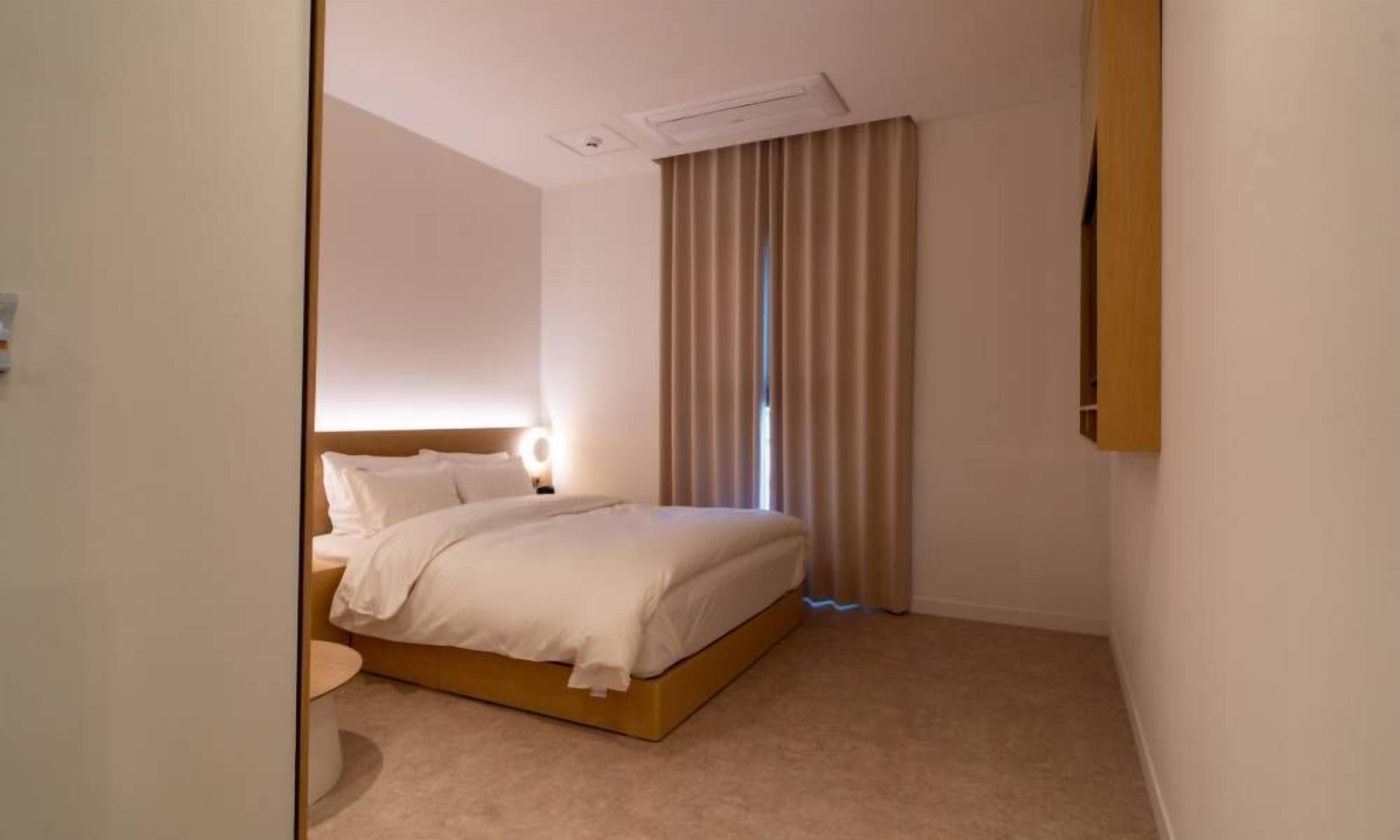 Een hotelkamer met een bed, nachtkastje, een tv aan de muur en een raam met gordijnen.