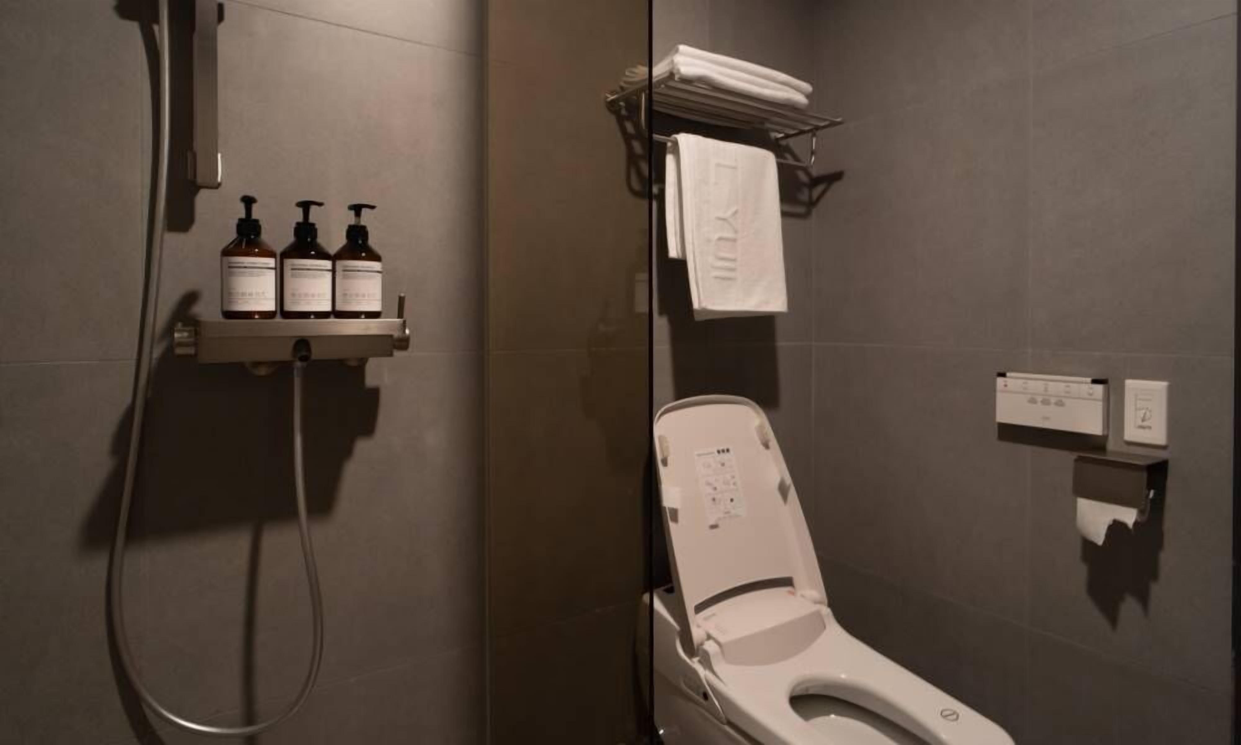 Un baño moderno con ducha, inodoro y un estante con artículos de aseo.