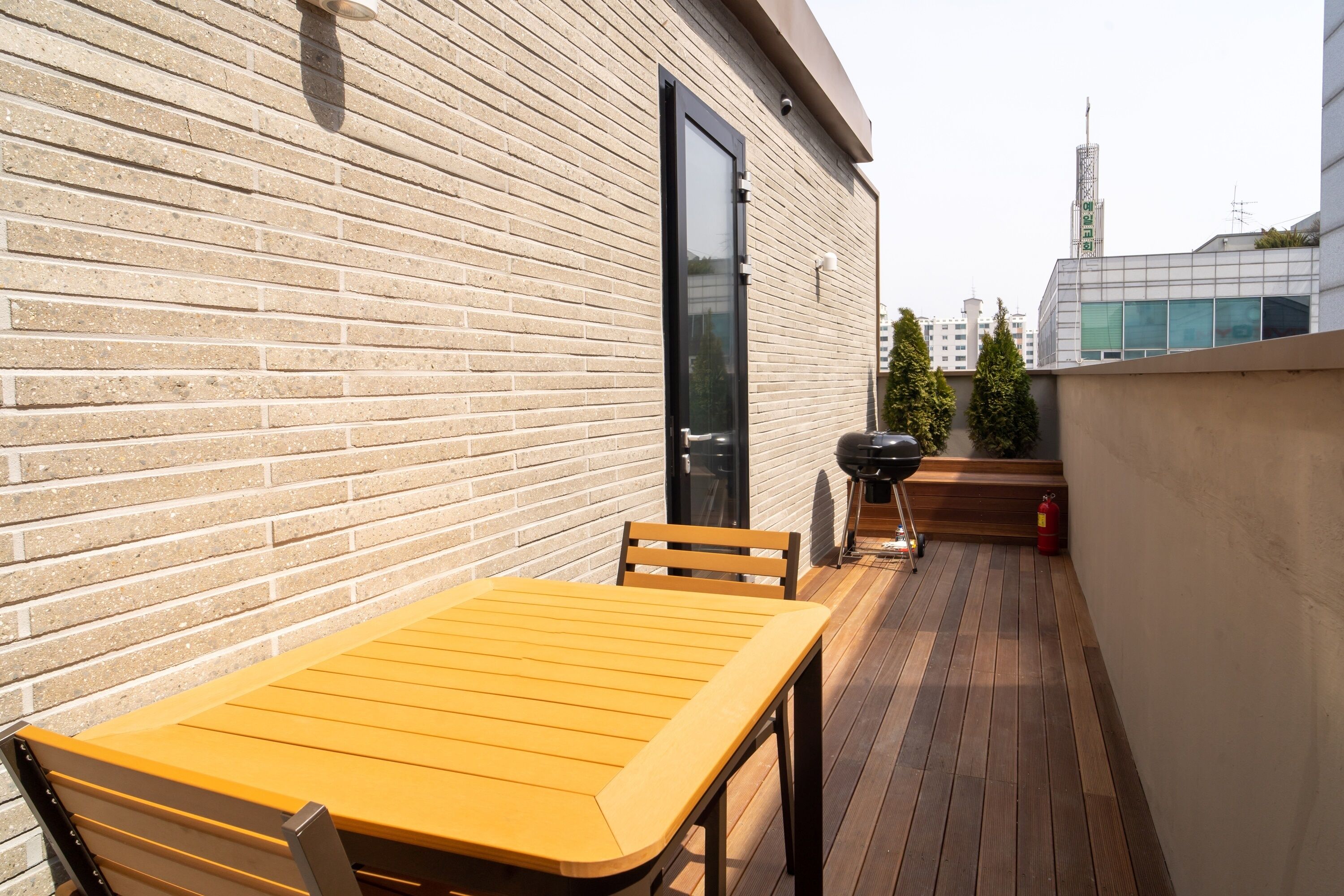 A wooden deck with a table and chairs, a barbecue grill, and a fire extinguisher.
