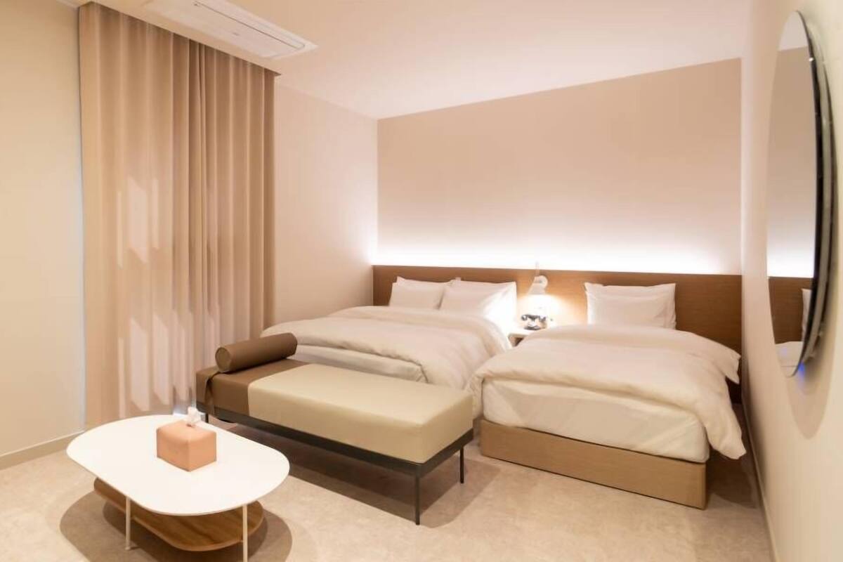 A hotel room with two beds, a small table, and a nightstand.