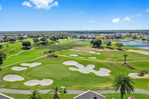 A golf course with bunkers, a bridge, and residential buildings in the background.