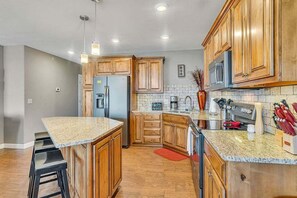 Eine moderne Küche mit Holzschränken, einer Granit Arbeitsplatte, Edelstahlgeräten und Barhocker.