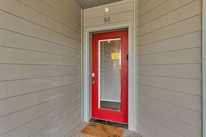 A red door with a number 14 above it, a doormat with "TAN" and "HEY" on it, and a small step leading to the door.