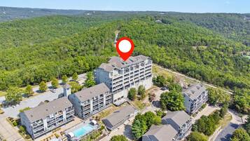 A multi-story hotel with a rooftop pool, surrounded by lush greenery and hilly terrain.