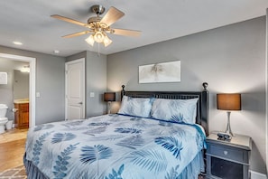 A bedroom with a bed, ceiling fan, bedside lamps, and a door leading to another room.
