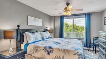 A bedroom with a bed, a nightstand, a dresser, a ceiling fan, and a window with curtains.